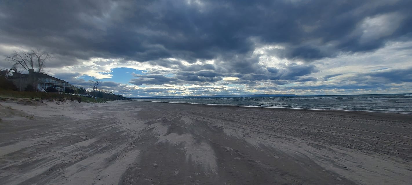 A landscape photo of a desolate looking beach with streaks of dry white sand over dark wet sand, big water broken by many whitecaps, and a sky that promises that winter is coming